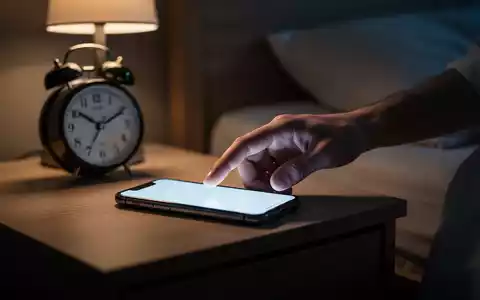 Eine Hand greift nach einem Smartphone auf einem Nachttisch in einem abgedunkelten Schlafzimmer, das digitale Erschöpfung symbolisiert. - Foto: über boerse-global.de