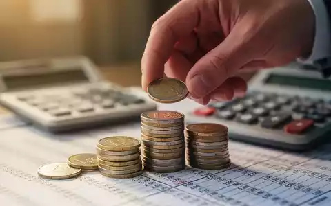 Eine Hand legt sorgfältig Euro-Münzen auf einen Stapel, mit einem unscharfen Finanzbuch im Hintergrund, das Sparen bei steigenden Zinsen symbolisiert. - Foto: über boerse-global.de