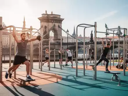 Menschen trainieren an modernen Fitnessgeräten in einem Park in Prag, im Hintergrund ist eine historische Brücke zu sehen. - Foto: über boerse-global.de