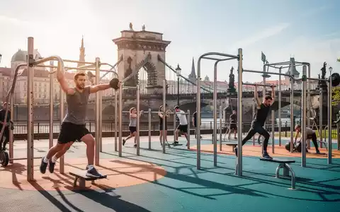 Menschen trainieren an modernen Fitnessgeräten in einem Park in Prag, im Hintergrund ist eine historische Brücke zu sehen. - Foto: über boerse-global.de