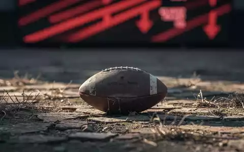 Ein deflatierter American Football liegt auf einem rissigen Feld, im Hintergrund ein unscharfer Aktien-Ticker mit roten Abwärtstrends. - Foto: über boerse-global.de