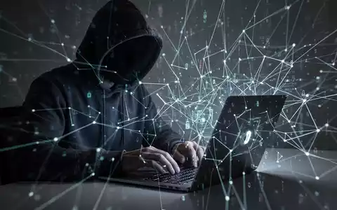 Person in Kapuzenjacke tippt auf Laptop, mit leuchtender digitaler Netzwerküberlagerung, symbolisiert Cybersicherheit und Bedrohungen. - Foto: über boerse-global.de