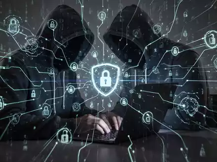 Verschattete Gestalt in Kapuzenjacke tippt auf Laptop, umgeben von leuchtenden digitalen Linien und abstrakten Netzwerksymbolen, die Cyberbedrohungen darstellen. - Foto: über boerse-global.de