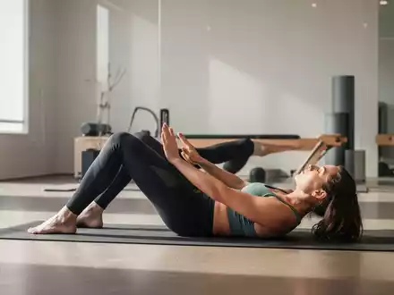 Eine Person führt eine Pilates-Übung auf einer Matte in einem modernen Studio aus, die die Rumpfmuskulatur und Beweglichkeit betont. - Foto: über boerse-global.de