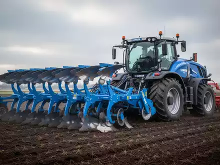 Eine große, moderne blaue Landmaschine steht ungenutzt auf einem Feld unter bewölktem Himmel, symbolisch für Kurzarbeit. - Foto: über boerse-global.de