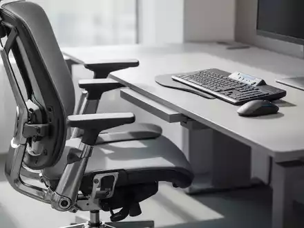 Ein ergonomischer Bürostuhl mit Synchronmechanik und eine kabellose, ergonomische Tastatur auf einem modernen Schreibtisch in einem Büroumfeld. - Foto: über boerse-global.de