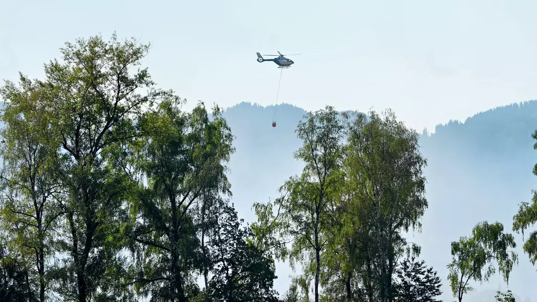 Ein Hubschrauber mit Löschwasser aus dem Chiemsee fliegt zu dem Brand. - Bild: Uwe Lein/dpa