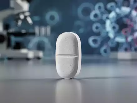 Eine einzelne pharmazeutische Pille liegt auf einer glatten Oberfläche, mit einem verschwommenen Hintergrund aus medizinischer Ausrüstung. - Foto: über boerse-global.de