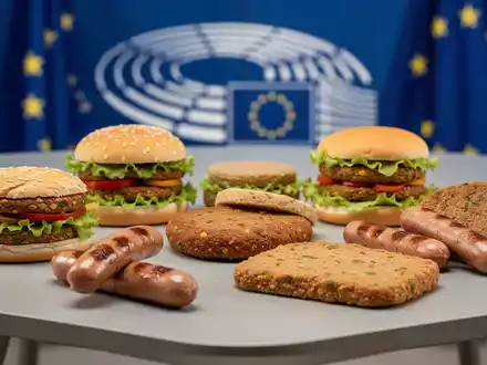 Eine Auswahl an pflanzlichen Fleischalternativen auf einem Tisch, im Hintergrund verschwommen die Farben der EU-Flagge. - Foto: über boerse-global.de