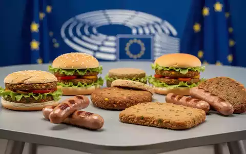 Eine Auswahl an pflanzlichen Fleischalternativen auf einem Tisch, im Hintergrund verschwommen die Farben der EU-Flagge. - Foto: über boerse-global.de