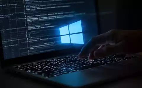 Eine Hand schwebt über einer Laptop-Tastatur, auf dem Bildschirm leuchtet ein blaues Windows-Logo und abstrakter Code. - Foto: über boerse-global.de
