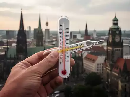 Ein Thermometer zeigt hohe Temperaturen an, im Hintergrund eine verschwommene deutsche Stadtlandschaft. Symbolisiert Hitzeschutzpflicht und finanzielle Belastung. - Foto: über boerse-global.de