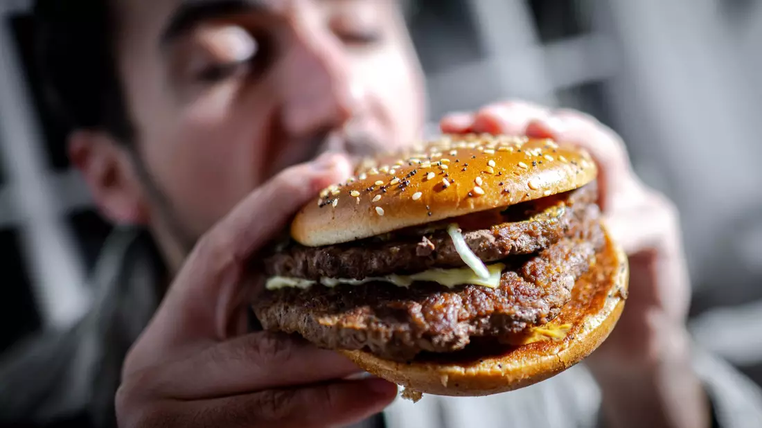 Illustration - Ein Mann beißt in einen Burger - Bild: Sina Schuldt/dpa/dpa-tmn