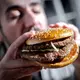 Illustration - Ein Mann beißt in einen Burger - Bild: Sina Schuldt/dpa/dpa-tmn