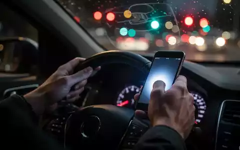 Nahaufnahme einer Hand, die ein Smartphone am Lenkrad hält, mit verschwommenem Straßenverkehr im Hintergrund. - Foto: über boerse-global.de