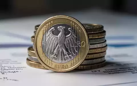 Nahaufnahme einer deutschen Euro-Münze mit Adler-Emblem, teilweise verdeckt von einem Münzstapel, vor verschwommenem Hintergrund. - Foto: über boerse-global.de