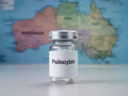 Ein kleines, versiegeltes Pharma-Behältnis mit der Aufschrift 'Psilocybin' auf einer sterilen Oberfläche, mit Australien im Hintergrund. - Foto: über boerse-global.de