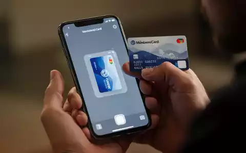 Eine Hand hält ein iPhone und scannt eine physische Karte, während die digitale Version auf dem Bildschirm in der Apple Wallet App erscheint. - Foto: über boerse-global.de