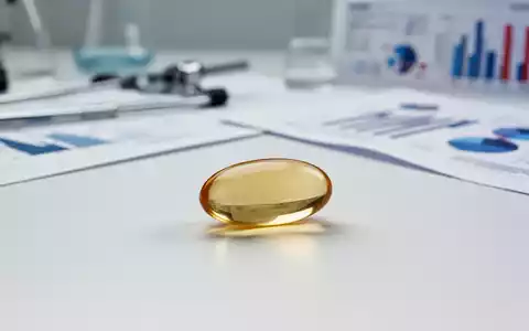 Eine einzelne glänzende Omega-3-Kapsel liegt auf einer sterilen weißen Oberfläche, im Hintergrund verschwommene wissenschaftliche Instrumente. - Foto: über boerse-global.de