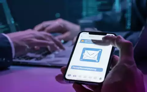 Nahaufnahme eines Smartphone-Bildschirms mit Phishing-Nachricht, unscharfer Hintergrund mit Händen, die auf Laptop tippen. - Foto: über boerse-global.de