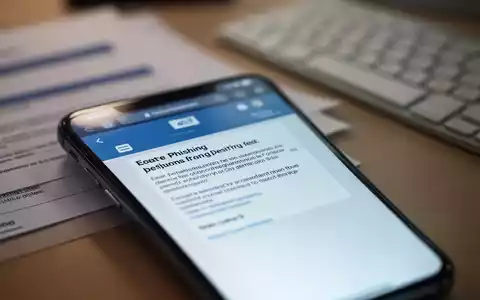 Nahaufnahme eines Smartphone-Bildschirms mit einer Phishing-E-Mail, im Hintergrund verschwommen ein Schreibtisch mit Dokumenten. - Foto: über boerse-global.de