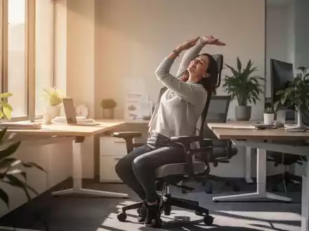 Eine Person macht eine kurze Dehnübung an einem modernen, ergonomischen Arbeitsplatz mit viel Tageslicht, um Bewegung und Wohlbefinden zu fördern. - Foto: über boerse-global.de