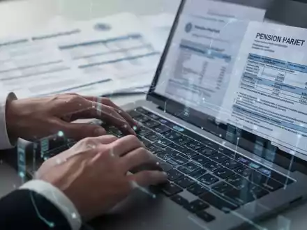 Hände tippen auf einem Laptop, im Hintergrund verschwommene Rentenunterlagen und Dokumente, symbolisiert digitale Rentenverwaltung. - Foto: über boerse-global.de