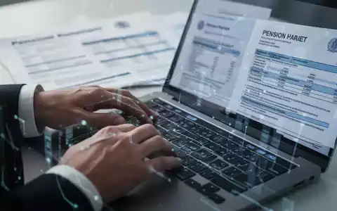 Hände tippen auf einem Laptop, im Hintergrund verschwommene Rentenunterlagen und Dokumente, symbolisiert digitale Rentenverwaltung. - Foto: über boerse-global.de