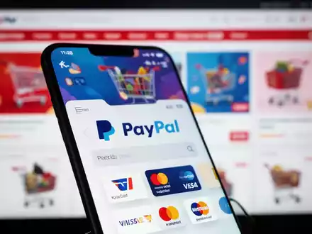 Ein Smartphone zeigt ein digitales Portemonnaie mit PayPal und anderen Zahlungsoptionen, im Hintergrund eine unscharfe E-Commerce-Website. - Foto: über boerse-global.de