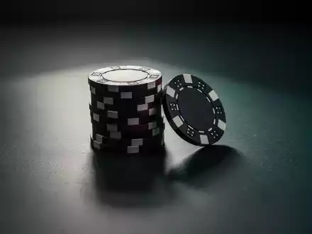 Ein einsamer, leicht geöffneter Stapel Pokerchips auf einer dunklen, reflektierenden Oberfläche, der einen Rückgang des Glücksspielmarktes symbolisiert. - Foto: über boerse-global.de