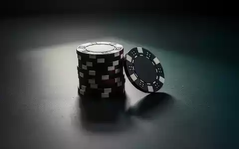 Ein einsamer, leicht geöffneter Stapel Pokerchips auf einer dunklen, reflektierenden Oberfläche, der einen Rückgang des Glücksspielmarktes symbolisiert. - Foto: über boerse-global.de
