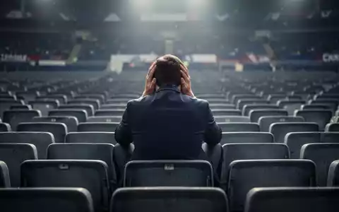 Ein einsamer Fußballfan sitzt enttäuscht mit dem Kopf in den Händen auf einem Stadionsitz, umgeben von leeren Reihen. - Foto: über boerse-global.de