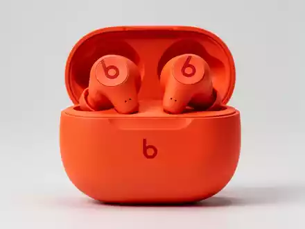 Nahaufnahme von leuchtend orangefarbenen Beats Solo Buds in der Ladehülle mit rotem 'b'-Logo auf sauberem Hintergrund. - Foto: über boerse-global.de