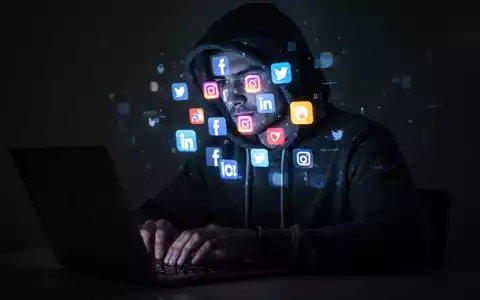 Eine Person im Kapuzenpullover tippt auf einem Laptop, mit leuchtenden Social-Media-Symbolen, die auf ihr Gesicht projiziert werden. - Foto: über boerse-global.de