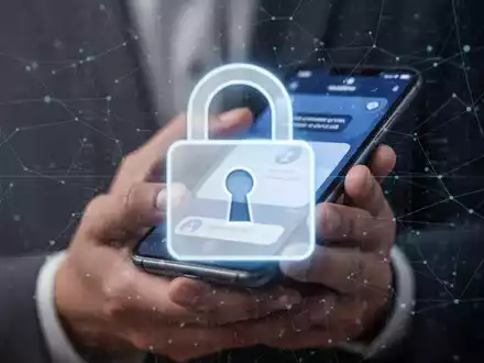 Ein stilisiertes, unscharfes digitales Vorhängeschloss-Symbol über der Nahaufnahme einer Hand, die ein Smartphone mit einer Benachrichtigung hält. - Foto: über boerse-global.de