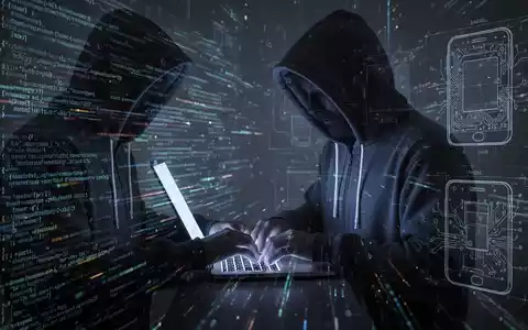 Verschattete Gestalt in Kapuzenjacke tippt auf Laptop, umgeben von digitalem Code und schwachen Blaupausen von Technikkomponenten. - Foto: über boerse-global.de