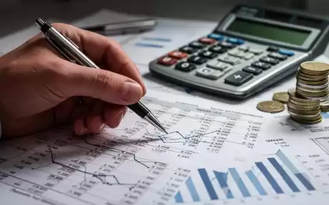 Eine Hand hält einen Stift über einem Finanzdokument mit Zahlen und Diagrammen, im Hintergrund ein Taschenrechner und Münzen. - Foto: über boerse-global.de