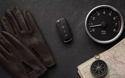 Flatlay mit Lederhandschuhen, Autoschlüssel, Tachoanzeige und Straßenkarte auf Schiefer. Mercedes-Benz Group AG, ISIN DE0007100000 - Foto: THN