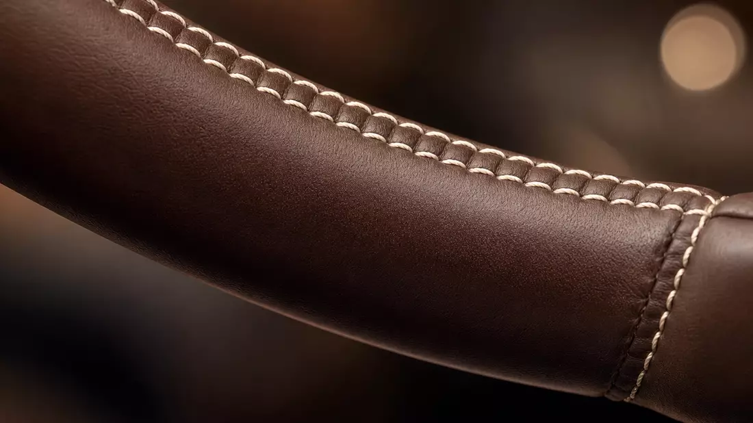 Extreme Nahaufnahme: dunkles Cognac-Nappaleder-Lenkrad mit feinen Doppelnähten und Bokeh-Hintergrund