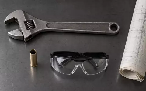 Rheinmetall AG (DE0007030009) Flatlay aus Schraubenschlüssel, leerer Hülse, Schutzbrille und Bauplan auf Holz - Foto: THN