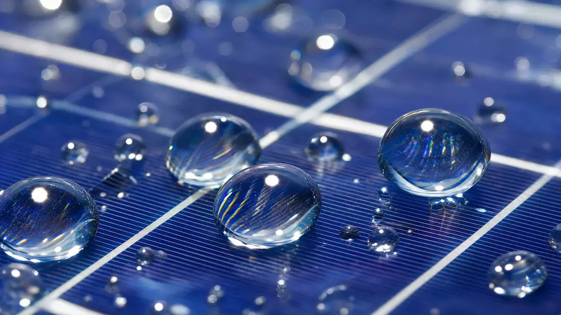 Makroaufnahme eines Solarpanels mit feinen Wassertropfen auf glatter Oberfläche.