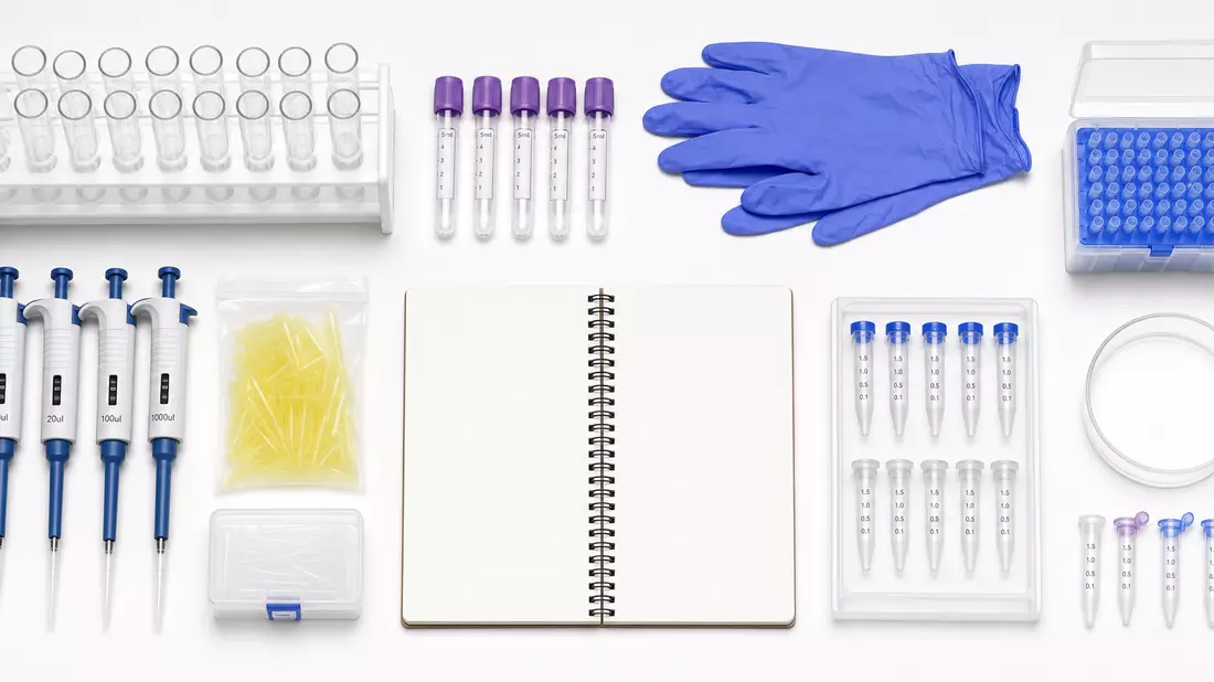 Flatlay aus Reagenzgläsern, Probenröhrchen, Handschuhen und Notizbuch auf weißem Tisch