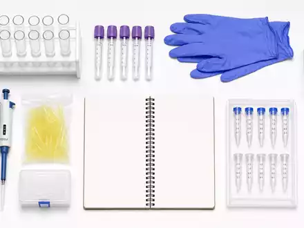 Qiagen N.V. (NL0012169213) Flatlay aus ReagenzglĂ€sern, Probenröhrchen, Handschuhen und Notizbuch auf weiĂem Tisch - Foto: THN