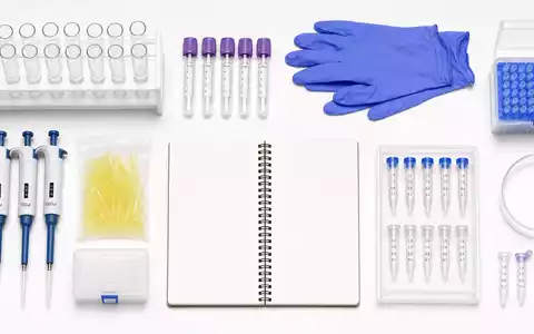 Qiagen N.V. (NL0012169213) Flatlay aus Reagenzgläsern, Probenröhrchen, Handschuhen und Notizbuch auf weißem Tisch - Foto: THN