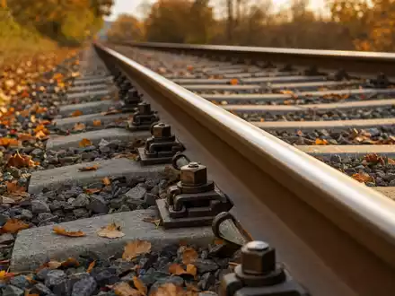 Vossloh AG (DE0007667107) zeigt Schienenbefestigungen auf herbstlichem Schotterbettgleis in goldenes Licht getaucht - Foto: THN