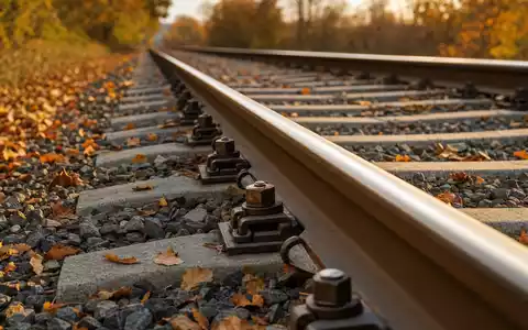 Vossloh AG (DE0007667107) zeigt Schienenbefestigungen auf herbstlichem Schotterbettgleis in goldenes Licht getaucht - Foto: THN