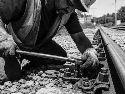 Vossloh AG (DE0007667107) dokumentiert Gleisarbeiter beim Schrauben an Schiene in schwarzweißem Reportagestil - Foto: THN