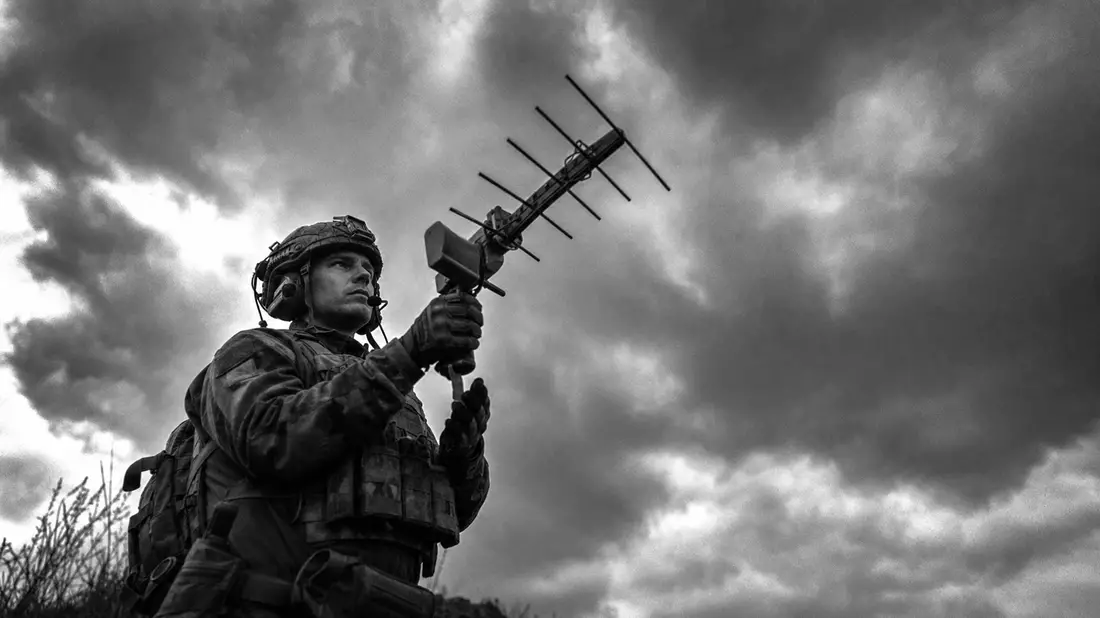 Soldat in Tarnausrüstung zielt Yagi-Antenne zum bewölkten Himmel, Schwarz-Weiß