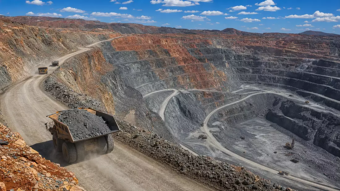 Tagebau-Mine mit gestuften Felswänden und schweren Muldenkippern im Tageslicht