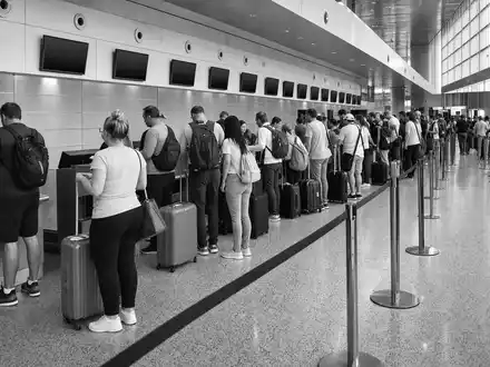TUI AG (DE000TUAG505): Dokumentarische Schwarzweiß-Aufnahme zeigt Reisende beim Check-in am belebten Flughafen-Schalter - Foto: THN